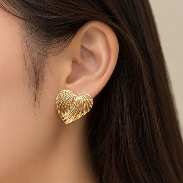 A close-up of a model's ear wearing a textured, ribbed gold heart-shaped stud earring.